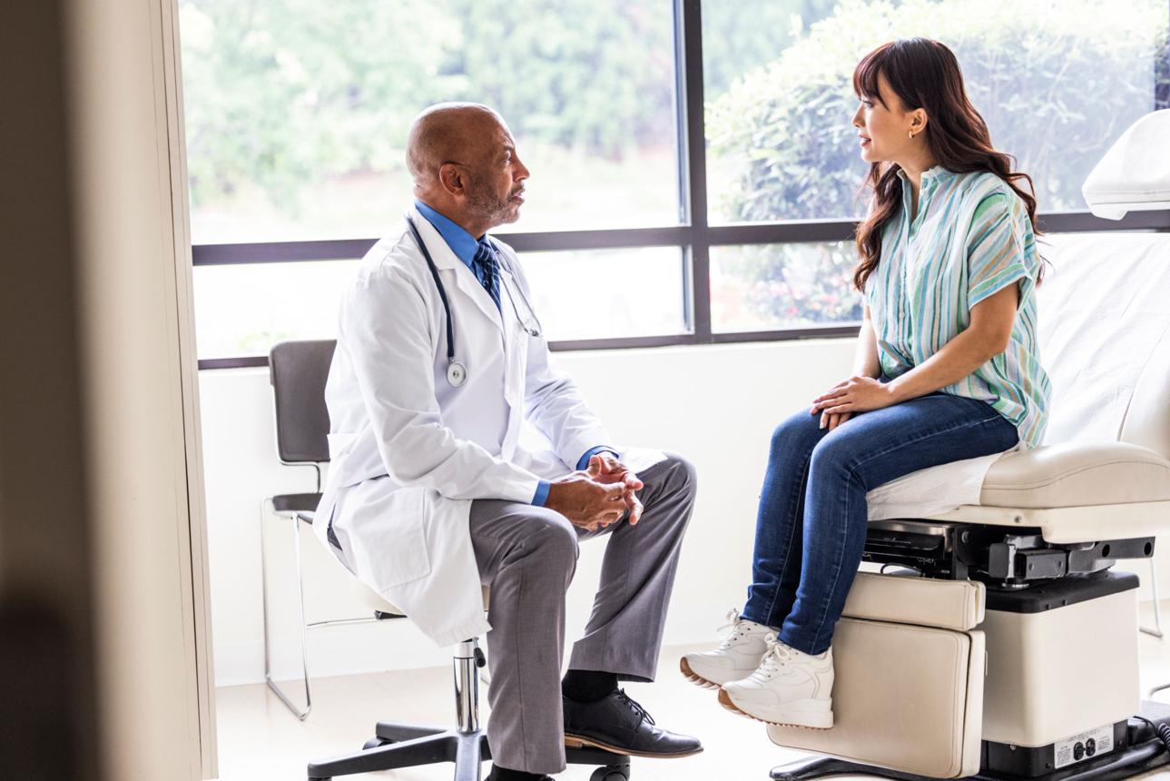 Male doctor talking with young woman in exam room